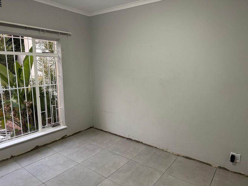 An empty bedroom featuring grey tiled flooring, security bars on the window, and unfinished wall-to-floor junctions requiring skirting board installation.