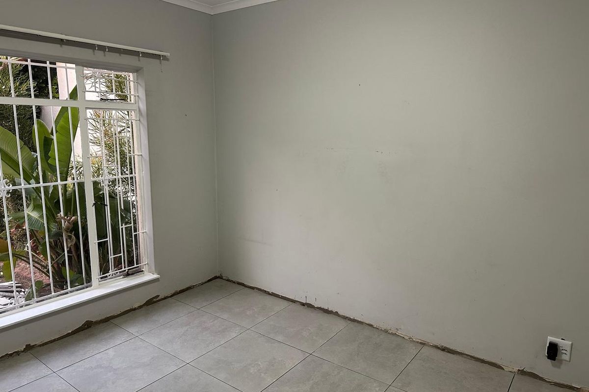 An empty bedroom featuring grey tiled flooring, security bars on the window, and unfinished wall-to-floor junctions requiring skirting board installation.