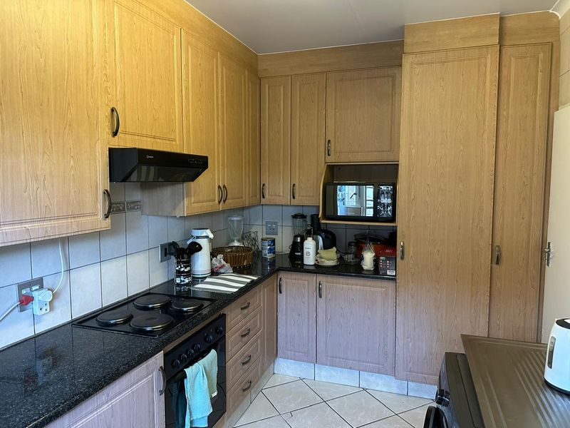A functional kitchen featuring light wood-look cabinetry, dark granite countertops, a built-in electric oven and hob, and tiled flooring.
