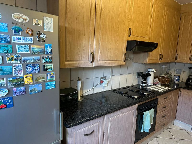 A functional kitchen featuring wood-look laminate cabinetry, granite countertops, a built-in oven, and an electric hob with an extractor fan.
