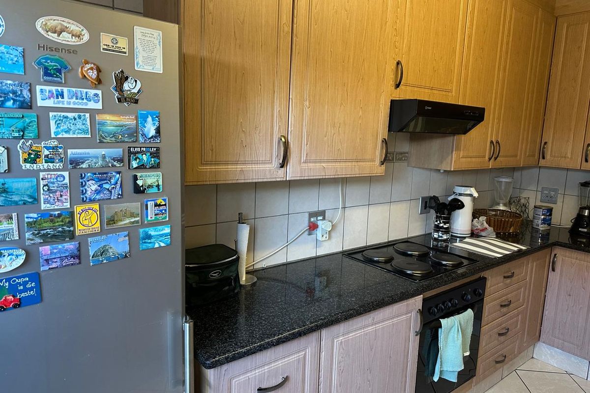 A functional kitchen featuring wood-look laminate cabinetry, granite countertops, a built-in oven, and an electric hob with an extractor fan.
