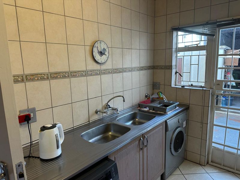 Functional laundry area featuring a double stainless steel sink, tiled splashback, built-in cabinetry, and direct access to the exterior via a security door.