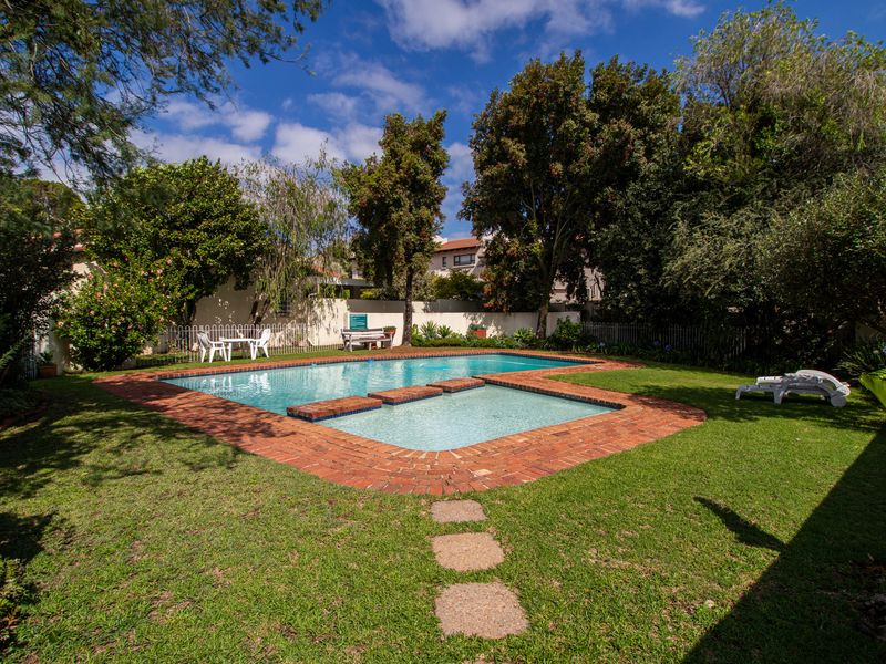 A private backyard featuring a swimming pool with brick coping, surrounded by a well-maintained lawn and mature garden landscaping.