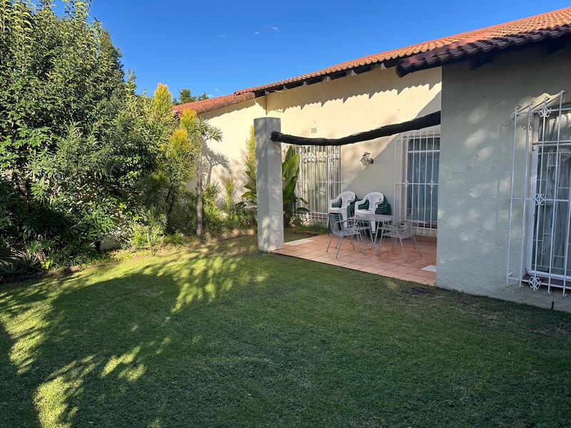 A rear view of the townhouse featuring a tiled patio area, security gates on windows, and a well-maintained private garden.