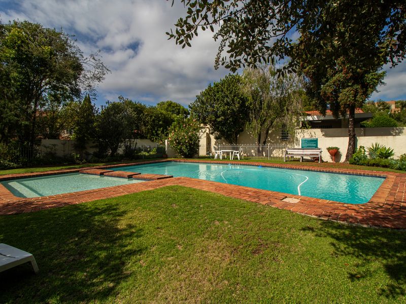 A well-maintained outdoor swimming pool area featuring brick coping, surrounding lawn, and established garden landscaping within a secure perimeter.