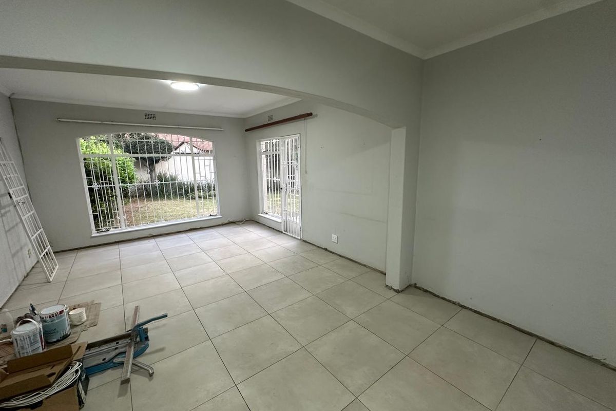 An empty, open-plan living area featuring large windows with security bars, tiled flooring, and an archway leading to an adjacent space.