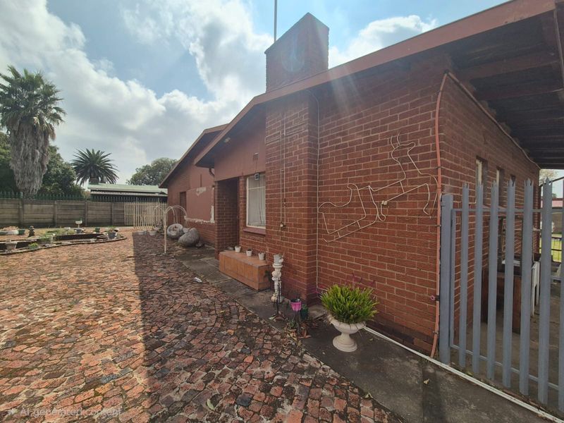 Rear exterior view of a brick house featuring a chimney, cobblestone paved courtyard, and steel security gate.