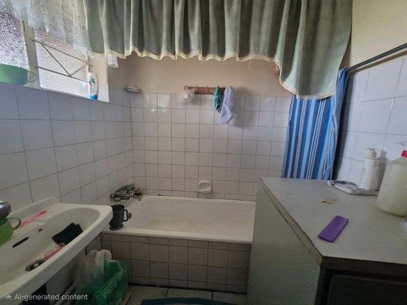 A functional bathroom featuring a standard bathtub, wall-mounted basin, and tiled finishes, offering potential for modernization and cosmetic updates.