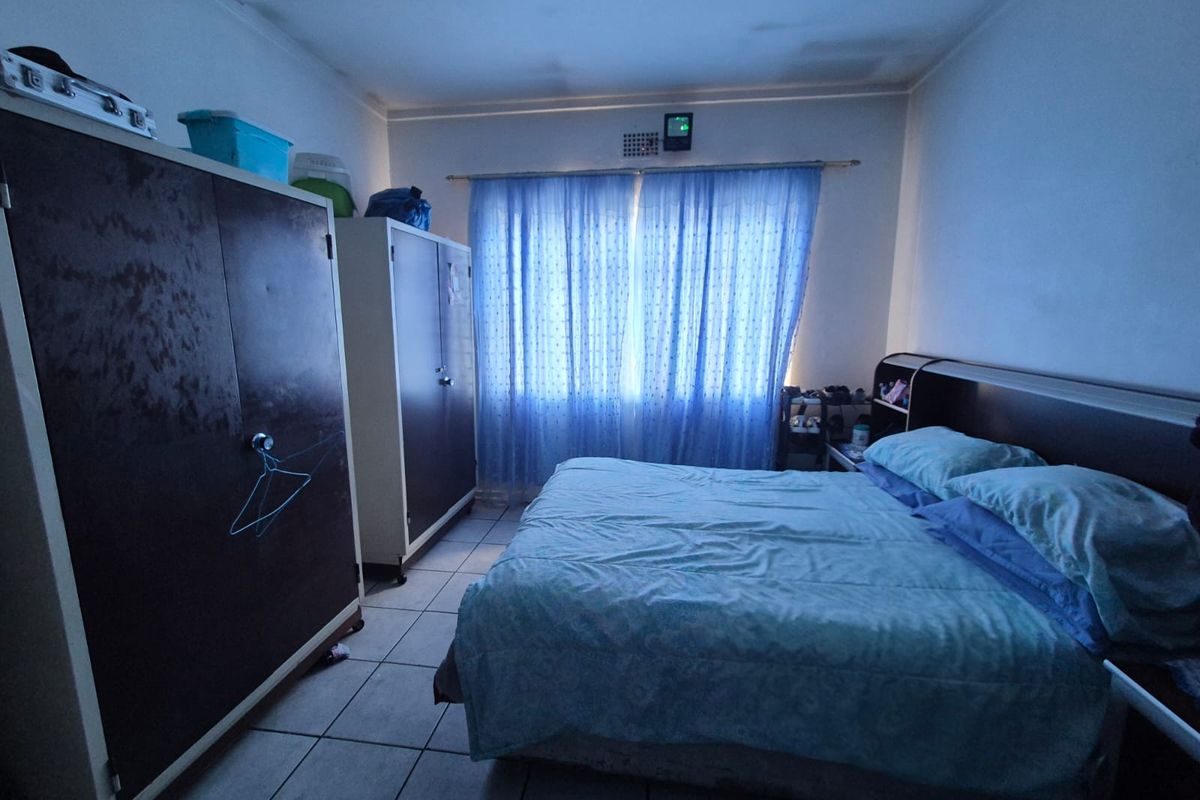 A bedroom featuring tiled flooring and curtain rails, showing signs of ceiling water damage and wear.