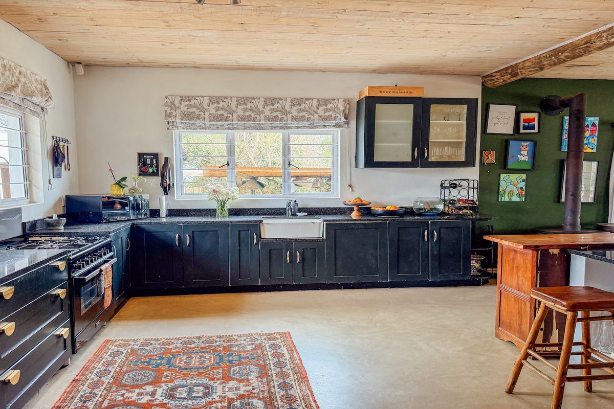 Spacious kitchen featuring dark cabinetry, granite countertops, a farmhouse sink, and a wood-burning fireplace, set under a rustic exposed timber ceiling.