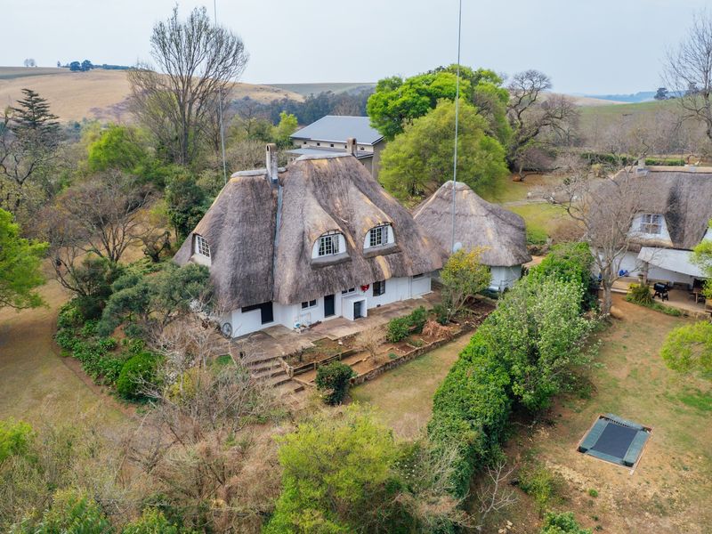 Aerial view of a rural small holding featuring multiple thatched-roof buildings set within a spacious, mature garden landscape.