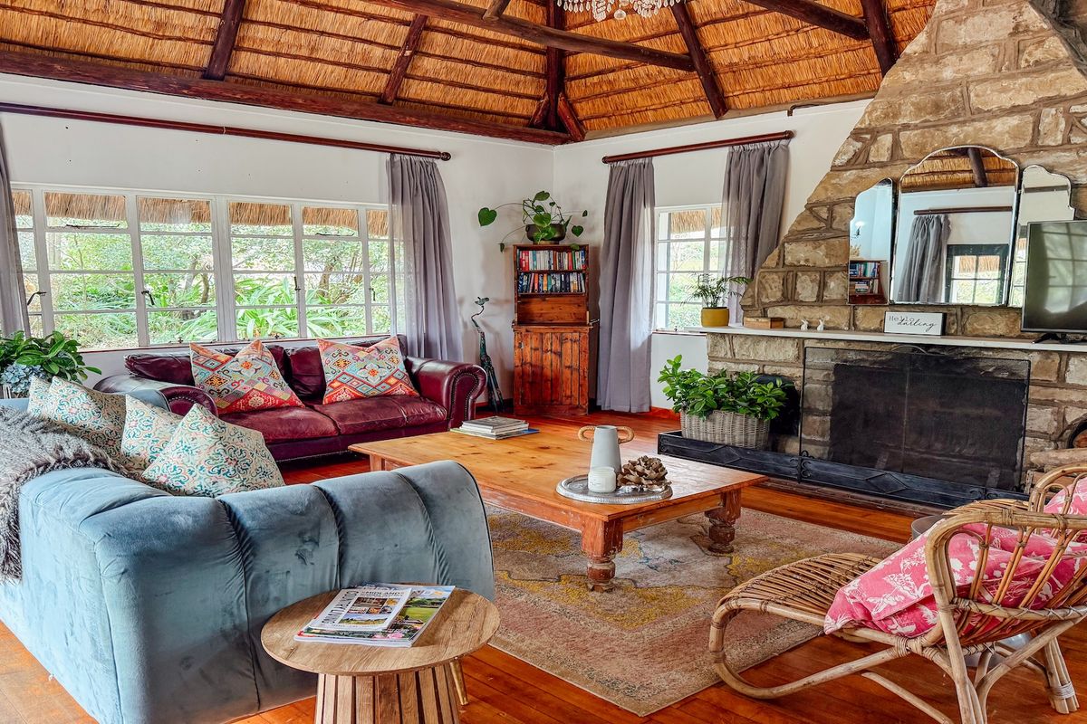 Spacious living room featuring a high thatched roof with exposed timber rafters, a prominent stone fireplace, and warm timber flooring.
