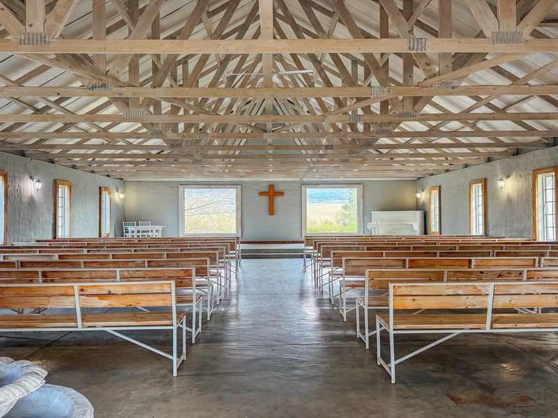 A spacious chapel or event hall featuring exposed timber roof trusses, polished concrete floors, and fixed wooden seating, offering a rustic and well-maintained interior.