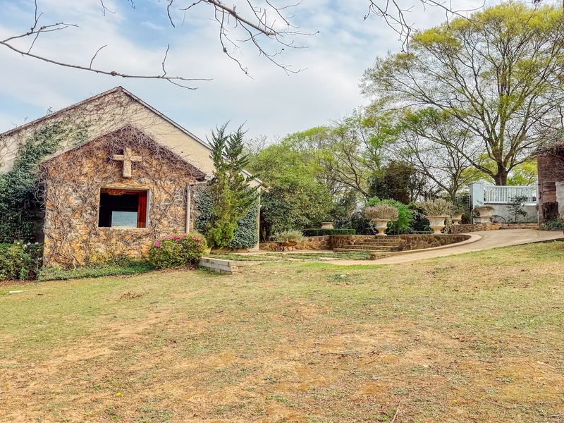A scenic view of the property grounds featuring a stone-clad building with a cross detail, stone retaining walls, and established garden landscaping.