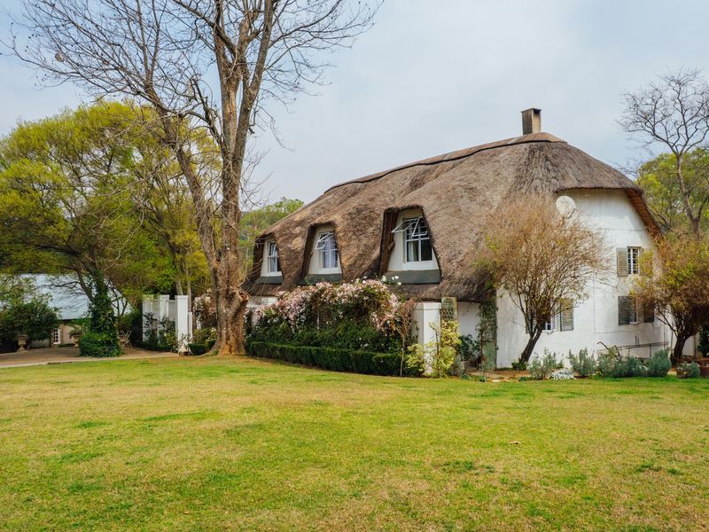 A charming thatched-roof cottage set within a spacious, well-maintained garden, featuring classic dormer windows and a traditional masonry exterior.