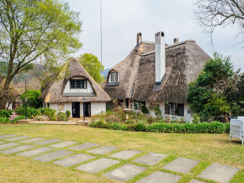 A charming thatched-roof cottage set within a well-maintained garden, featuring stone pathways and traditional architectural character.