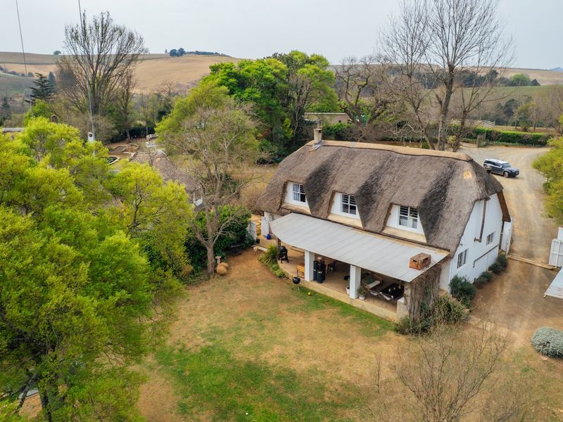 Aerial view of a rural small holding featuring a traditional thatched-roof dwelling with a covered patio and expansive surrounding grounds.