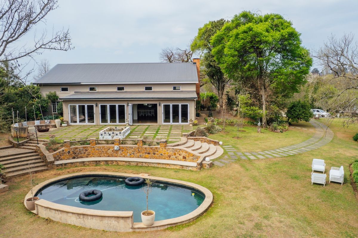 Aerial view of the rear exterior featuring a swimming pool, stone retaining walls, paved patio area, and large sliding glass doors leading into the home.