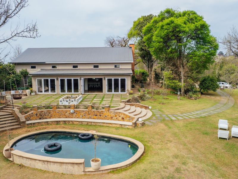 Aerial view of the rear exterior featuring a swimming pool, stone retaining walls, paved patio area, and large sliding glass doors leading into the home.