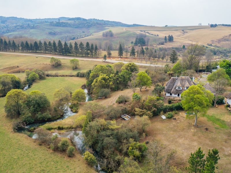 Aerial view of a small holding property featuring thatched roof dwellings, a winding river, and expansive surrounding rural landscape.
