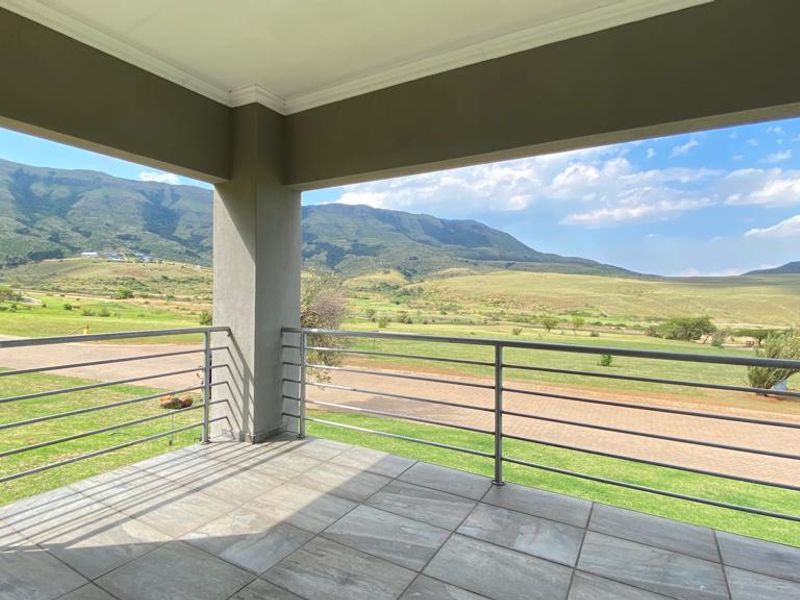 A covered balcony featuring tiled flooring and a metal balustrade, offering expansive views of the surrounding landscape and mountains.