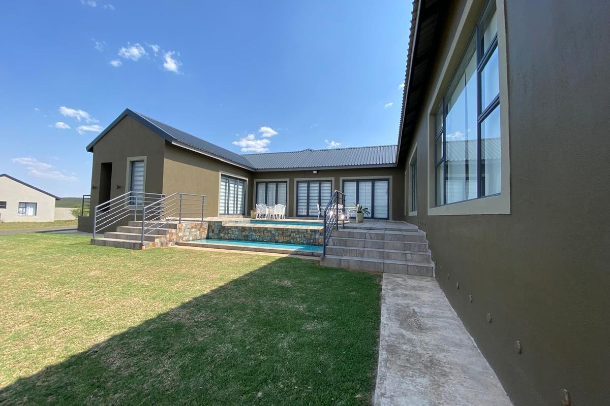 Rear view of the property featuring a swimming pool with stone cladding, tiled steps, and a well-maintained lawn area.