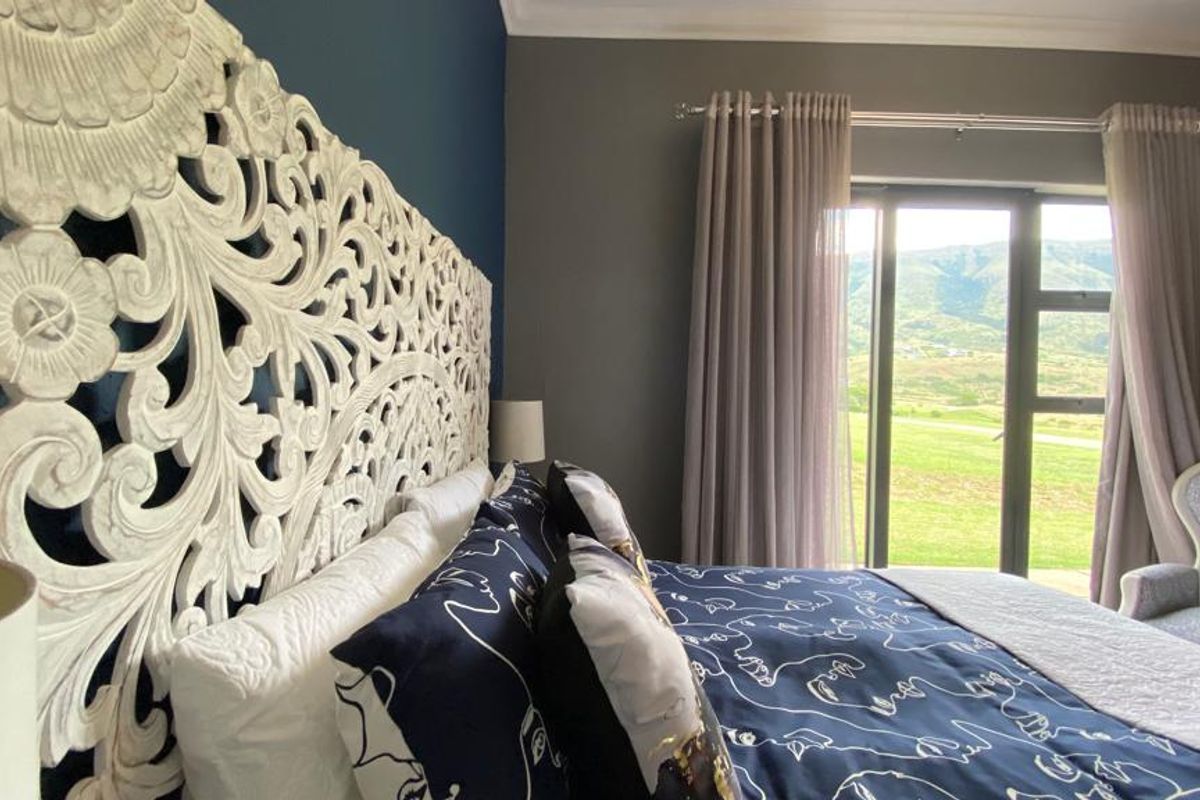 A well-maintained bedroom featuring dark accent walls, a large decorative headboard, and sliding glass doors providing natural light and scenic outdoor views.