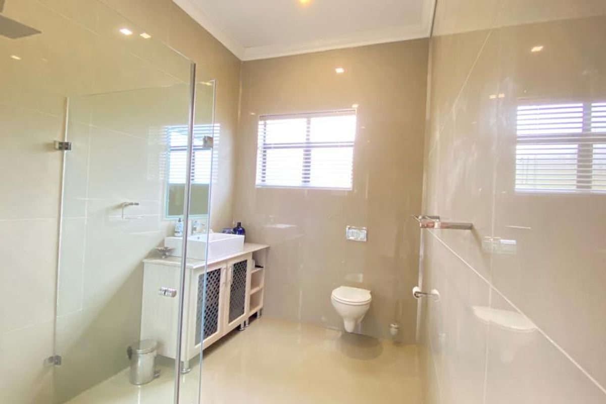 Modern bathroom featuring a glass-enclosed rain shower, wall-mounted toilet, and a vanity with a vessel sink, finished with neutral wall and floor tiles.