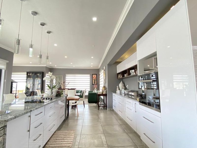 Modern open-plan kitchen and living area featuring high-gloss cabinetry, stone countertops, integrated appliances, and elegant pendant lighting throughout the spacious, well-lit interior.