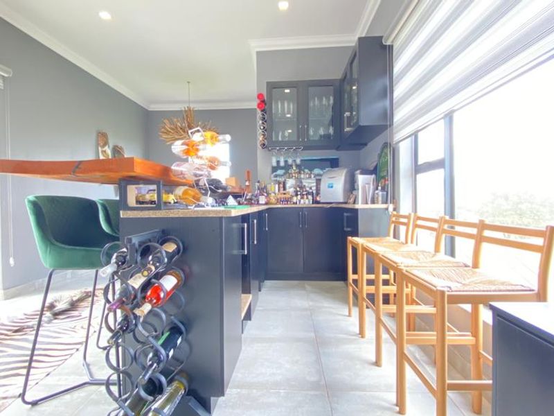 A modern home bar area featuring dark cabinetry, a stone countertop, integrated wine storage, and large windows providing ample natural light.