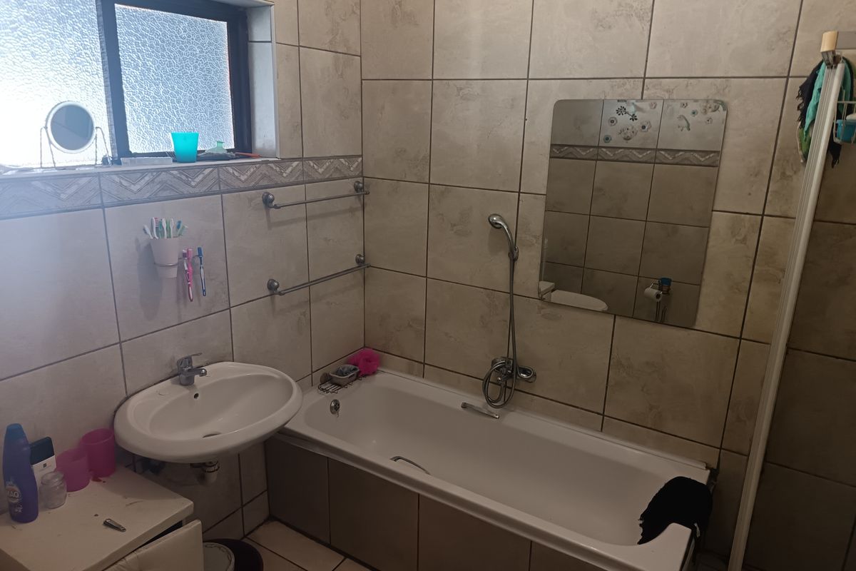 A functional bathroom featuring a built-in bathtub with handheld shower mixer, wall-mounted basin, and neutral tiled finishes throughout.
