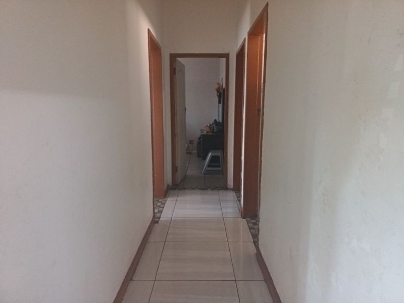 A narrow residential hallway featuring tiled flooring and wooden door frames, showing signs of wear on the walls.