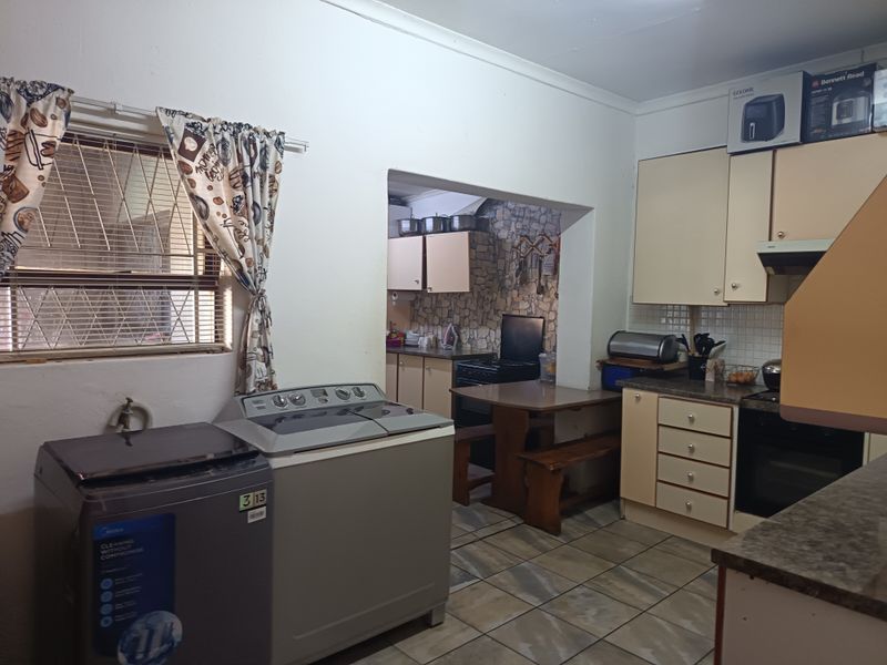 A functional kitchen and laundry area featuring built-in cabinetry, tiled flooring, and integrated cooking appliances, offering potential for modernization.