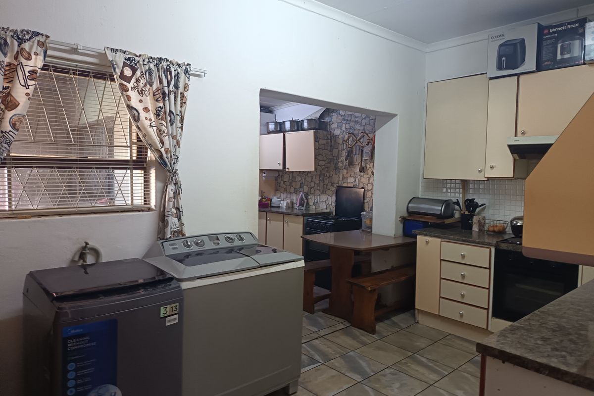 A functional kitchen and laundry area featuring built-in cabinetry, tiled flooring, and integrated cooking appliances, offering potential for modernization.