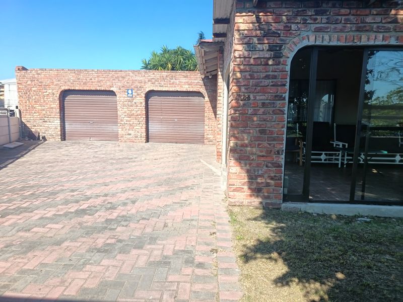 Exterior view of a townhouse featuring a double garage with roller doors, brick facade, and a paved driveway leading to the entrance.