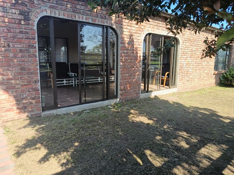 Rear view of a townhouse featuring exposed brick walls, arched sliding glass doors, and a paved patio area overlooking a garden.