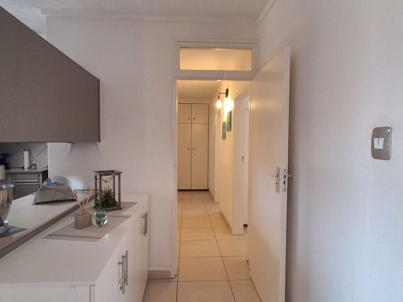 A bright hallway featuring tiled flooring, built-in storage cabinetry, and a transom window above the doorway leading to the interior living spaces.