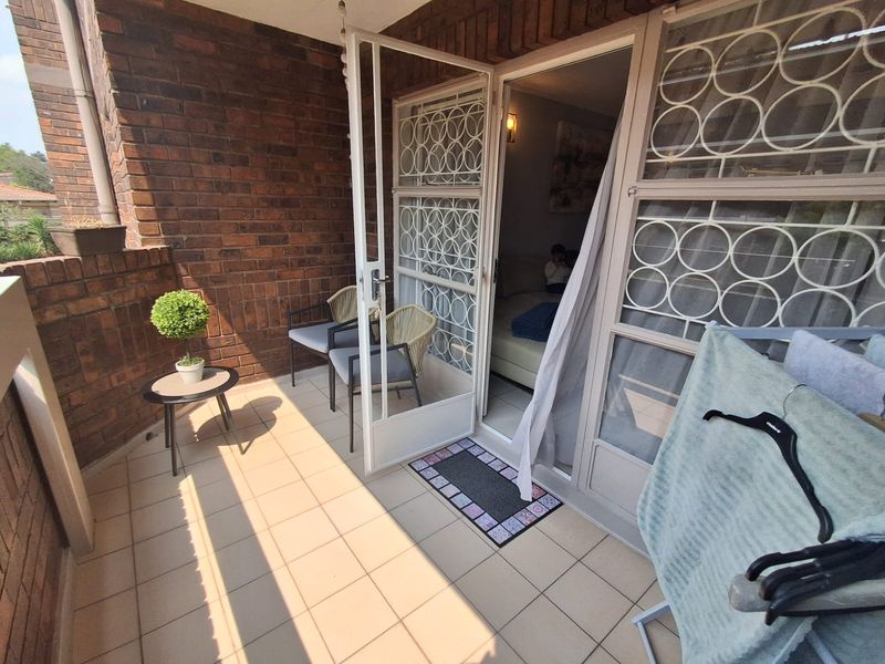 A covered balcony featuring brick walls, tiled flooring, and a secure metal gate providing access to the interior living space.