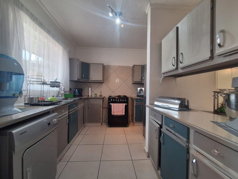 A functional kitchen featuring tiled flooring, ample built-in cabinetry, a tiled splashback, and a freestanding stove, offering a practical layout for daily cooking.