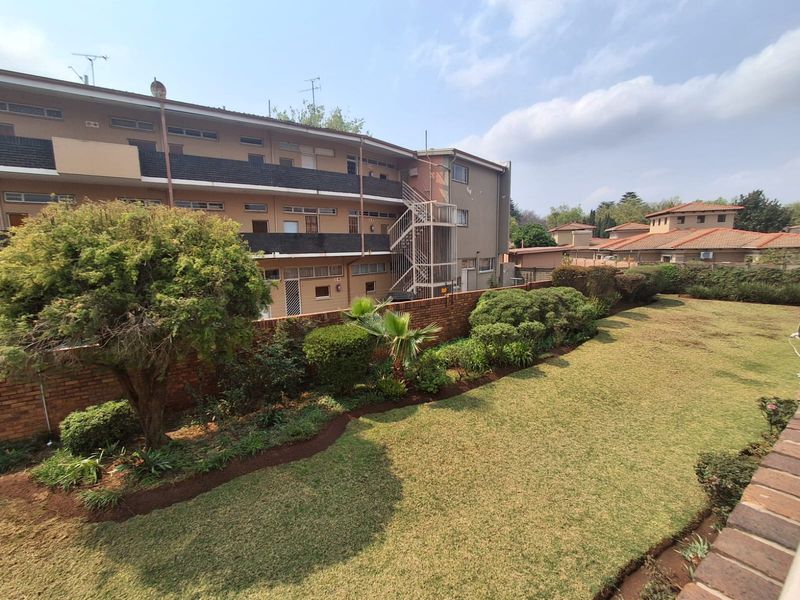 View of the rear communal garden area and the exterior facade of the apartment building featuring a brick boundary wall and metal staircase.