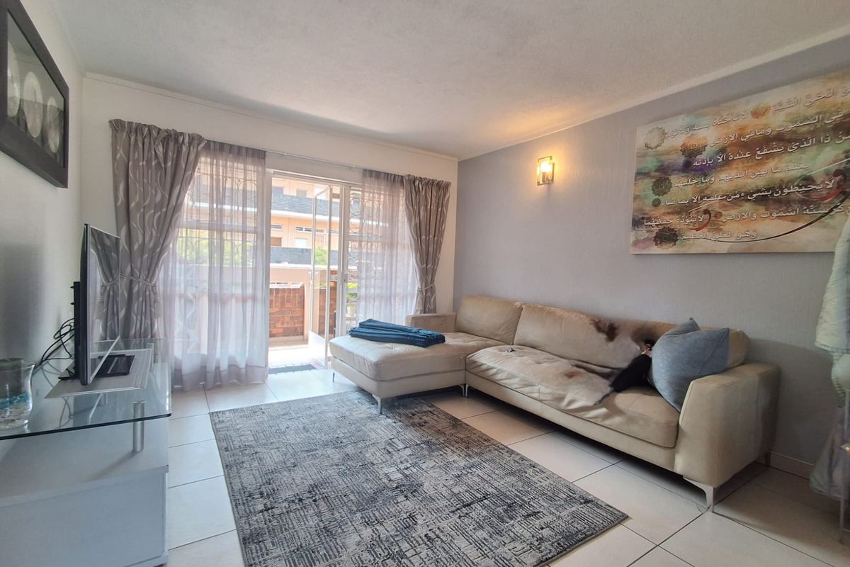 A bright living room featuring tiled flooring, wall sconce lighting, and a sliding glass door providing access to an outdoor balcony area.