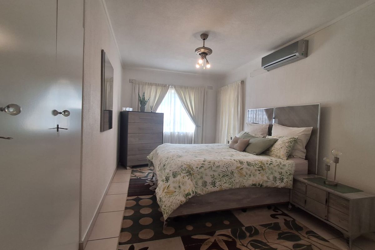 A well-maintained bedroom featuring tiled flooring, built-in cupboards, and a wall-mounted air conditioning unit.