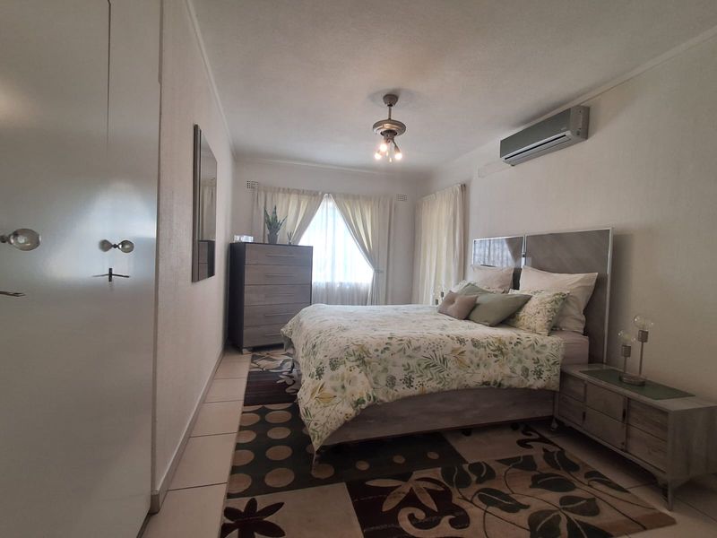 A well-maintained bedroom featuring tiled flooring, built-in cupboards, and a wall-mounted air conditioning unit.