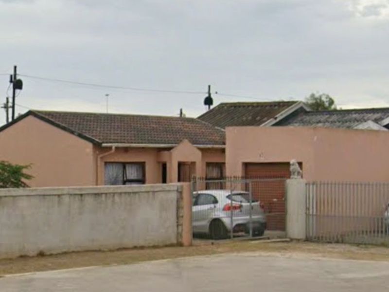 Front elevation of a single-story house featuring a tiled roof, perimeter wall, and gated driveway access.