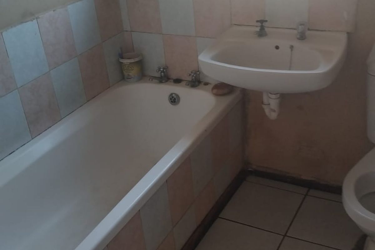 A functional bathroom featuring a standard bathtub, wall-mounted basin, and tiled finishes, currently requiring cosmetic updates and maintenance.