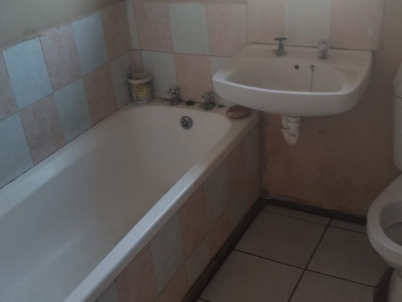 A functional bathroom featuring a standard bathtub, wall-mounted basin, and tiled finishes, currently requiring cosmetic updates and maintenance.