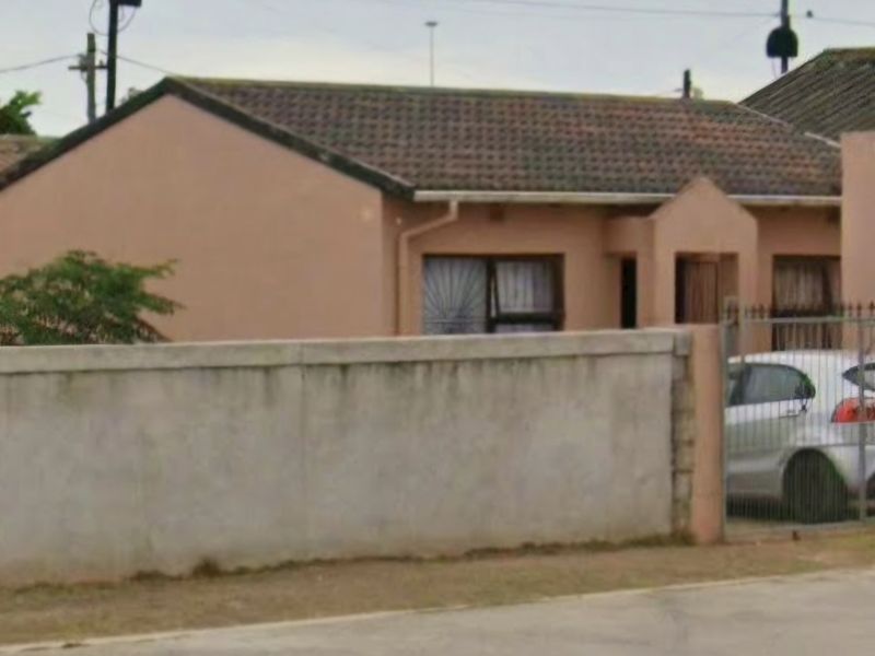 Front view of a single-story residential house featuring a tiled roof, perimeter wall, and gated entrance.