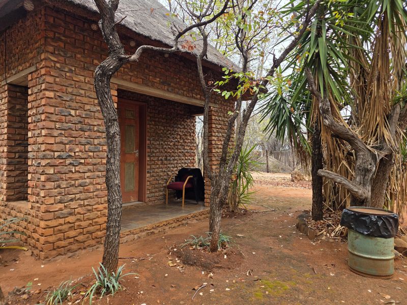 A rustic farm-style cottage featuring exposed brick walls, a traditional thatched roof, and a small tiled porch entrance.