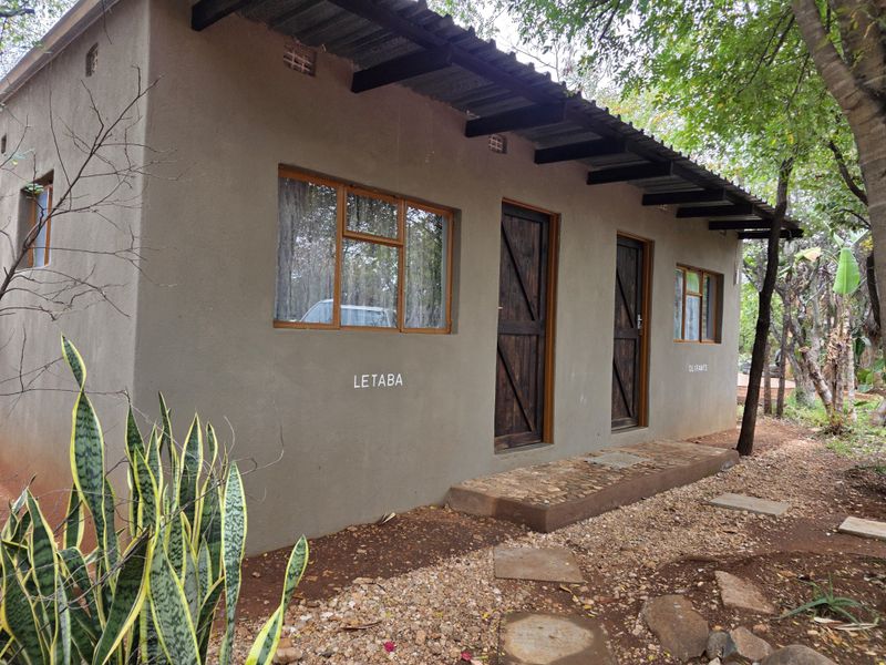 Exterior view of a rustic farm-style building featuring a corrugated metal roof, timber-framed windows, and wooden doors with a stone-paved entrance path.