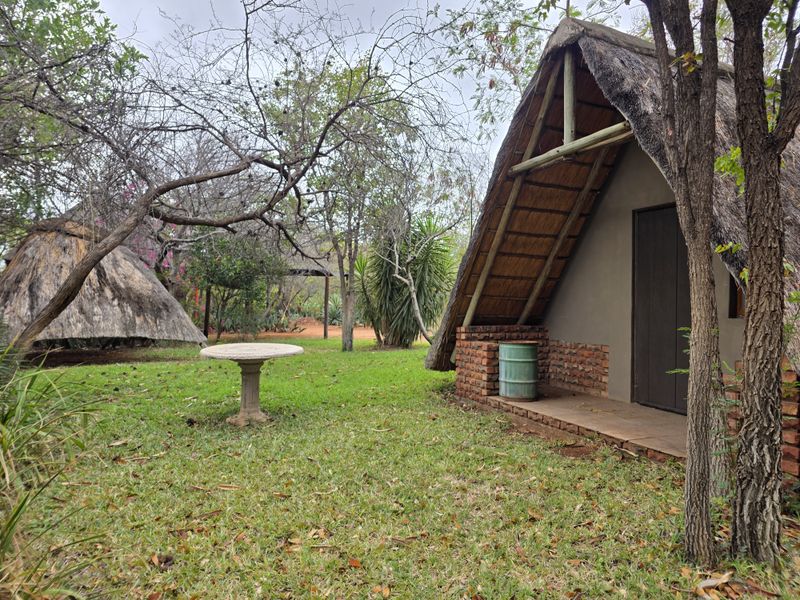 A rustic farm-style cottage featuring a traditional thatched roof and exposed brick exterior, set within a landscaped garden area.